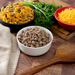Cheesy beef pasta, shredded cheddar cheese, cooked ground beef, and fresh parsley on a wooden table.