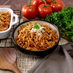 Cheesy lasagna pasta in a bowl, garnished with cheese and parsley, with fresh tomatoes and herbs nearby.