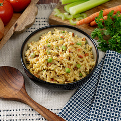 Creamy rotini pasta with peas and vegetables in a black bowl, surrounded by fresh carrots, celery, parsley, and tomatoes.