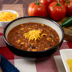 Hearty tortilla soup in bowl topped with shredded cheddar, fresh tomatoes and jalapeños nearby