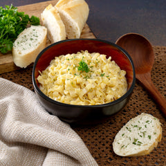 Creamy Alfredo pasta in a black bowl with parsley, served with sliced bread and wooden spoon