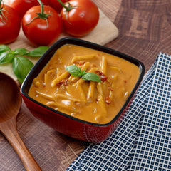 Tomato basil soup with pasta in a red bowl, fresh tomatoes and basil on wood table
